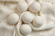 © mikeosphoto - Six wool dryer balls placed on a soft, textured white knitted blanket, top view, flat lay. An eco-friendly, reusable alternative for reducing static and wrinkles in laundry