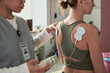 © pressmaster - Healthcare professional using TENS unit on patient's back during physical therapy session. Electrode pads applied to patient's back for muscle stimulation and pain relief