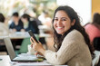 © Jannik - A smiling business woman using her phone while sitting at the table in a modern office