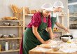 © JackF - Skilled two baker in apron, adult female and young guy kneading dough, cutting and weighing portioned pieces on floured surface before baking in kitchen