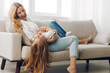 © SHOTPRIME STUDIO - Mother and daughter sharing a joyful moment on a cozy couch in a bright, white living room with minimalistic decor