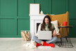 © Pixel-Shot - Young woman using laptop near armchair at home on winter day