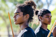 © Caseyjadew - Two young men intensely focus with sticks at outdoor cultural event under bright sun.
