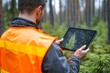 © app - Forester in Orange Vest Using Tablet to Analyze Forest Map in Lush Green Environment