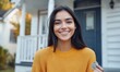 © VINA - A smiling woman in a yellow sweater holds a key outside a house.