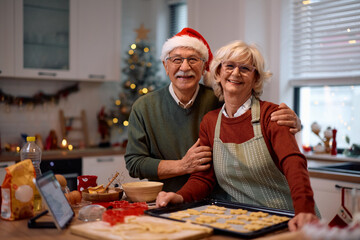 Wall Mural - Happy senior couple baking Christmas cookies and looking at camera.