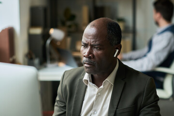 Poster - Serious mature director of company or ceo with earphones looking at computer screen while concentrating on financial analysis