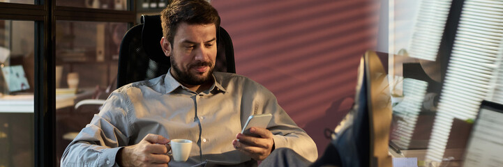 Aufkleber - Banner of manager with cup of coffee texting in smartphone while sitting in armchair and keeping crossed legs on workplace