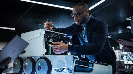 Fototapete - African Engineer Using a Screwdriver While Developing a Remotely Controlled Delivery Robot. Black Specialist Working in High Tech Research Laboratory with Modern Equipment