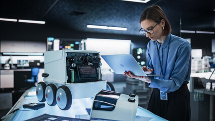 Fototapete - Portrait of a Female Engineer Using a Laptop While Developing a Remotely Controlled Delivery Robot.Technical Specialist Working in High Tech Research Laboratory with Modern Equipment