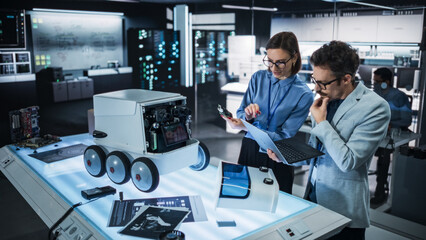 Leinwandbilder - Portrait of Two Colleagues Working in a Research Facility, Using Laptop Computer to Develop a Futuristic Robot for Autonomous Deliveries. Engineers Working on Improving Detectors on their Prototype 
