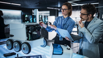 Leinwandbilder - Portrait of Two Colleagues Working in a Research Facility, Using Laptop Computer to Develop a Futuristic Robot for Autonomous Deliveries. Engineers Working on Improving Detectors on their Prototype 