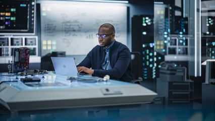 Fototapete - Portrait of an African Male Specialist Using Laptop Computer to Improve Electronic Circuit Board in Modern Office. Black Engineer Thinking and Typing Ideas for Artificial Intelligence Project 
