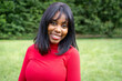 © Lomb - Beautiful young African American woman smiling outdoor wearing red sweater against blurred green park setting