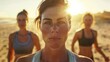 © iuricazac - A woman in her 40s with brown hair pulled back wearing a white sports bra stands in front Of two women in Sports bras with the Sun shining brightly behind them likely On a beach.