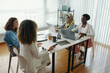 © DragonImages - Four professional women engaging in collaborative work at table with laptops and documents while discussing. Sunlight coming through blinds illuminating workspace