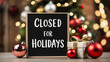 © KF - Closed for holidays sign board on a wooden table, with festive decor in background. perfect for business, retail store, office
