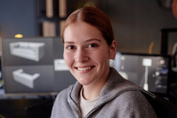 Fototapete - Portrait of woman smiling warmly while working in modern office setting with computer screens displaying design software behind her