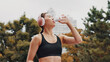 © peopleimages.com - Drinking water, outdoor and woman with fitness, healthy and wellness with workout. Japanese person, runner and athlete in city, headphones and listening to music, sound and thirsty with hydration