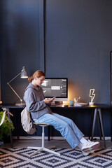 Poster - Person engrossed in laptop with desk displaying computer monitor, books, and lightning shape lamp sitting in modernly decorated home office with geometric patterned rug while wearing casual attire