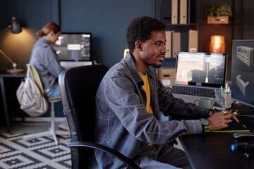 Leinwandbilder - Man concentrating on computer with tablet and coffee while woman in background working on desktop. Office filled with modern technology and organized workspace