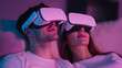 © MonkaLemonka - young couple sitting togethee on sofa, resting during using virtual reality goggles isolated over dark pink house interiors; copy space
