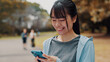 © peopleimages.com - Smile, woman and typing with phone of fitness outdoor, communication and research of exercise application. Happy, athlete and mobile for gym membership, training schedule and workout routine in Japan