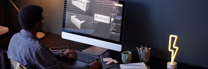 Fototapete - Man sitting at desk, analyzing 3D architectural models on computer screen, surrounded by office supplies, with focus on design tasks
