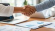 © acnaleksy - business shaking hands with a client over a conference table, with documents and a laptop