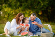 © GRON777 - Happy family enjoying picnic in park. Parents with girl eating watermelon sitting on blanket on grass on hot summer day. Family, leisure, healthy eating concept