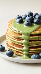 Wall Mural - Fluffy matcha pancakes topped with blueberries and green drizzle on a neutral background