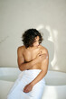 © AnnaStills - Vertical shot of topless man with towel around his waist sitting on bath and applying lotion