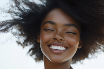 Wall Mural - A joyful young woman with natural hair smiling brightly against a light background.