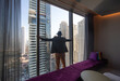 © serikbaib - man in hotel room looking out window at skyscrapers