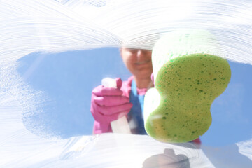 Wall Mural - Woman washing window with sponge against blue sky, closeup