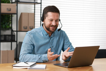 Wall Mural - Interpreter in headset having video chat via laptop at wooden table indoors