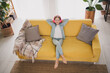 © deagreez - Adorable girl in casual denim attire enjoying music with headphones while relaxing on a cozy yellow sofa at home during daylight hours