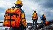 © khonkangrua - Rescue Team Members in Bright Safety Gear at Rocky Beach Under Overcast Sky, Preparing for Emergency Operations Near the Shoreline