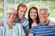 © peopleimages.com - Hug, portrait and smile of big family in living room of home together for bonding, love or visit. Happy, relax or wellness with group of men and women in apartment for support, trust or wellness