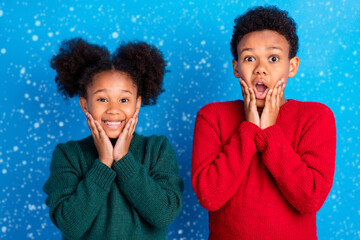 Wall Mural - Photo of sweet impressed dark skin children wear pullover smiling arms cheeks isolated blue color background