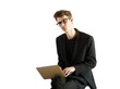 © peshkova - A young man in glasses and asuit working on a laptop, seated casually on a white background. Concept of work, business, technology