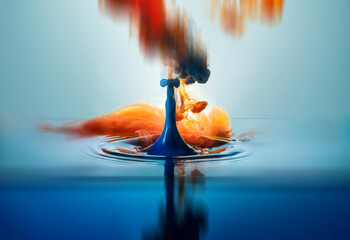 Poster - A blue droplet falls into water, creating a vibrant explosion of orange and red colors. The resulting splash and ripples are captured in a stunning, abstract image.  The colors blend and swirl, reflec
