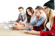 © peshkova - Group of young professionals collaborating on a project, using a laptop and documents, sitting at a desk, on a white background, teamwork concept