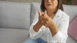 © Krakenimages.com - A middle-aged hispanic woman with short hair wearing glasses holds her sore hand while sitting in her living room.