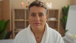 © Krakenimages.com - Young man in a spa wellness center wearing a white bathrobe indoors with a calm expression amidst a serene, candlelit background.