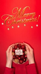 Wall Mural - Hands holding a festive basket with red Christmas ornaments and a small gift on a vibrant red background.