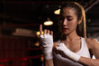 © kamonrat - Confident Female Boxer Wrapping Hands in Gym, Preparing for Training Session, Strong and Determined, Focused Athlete in Boxing Environment, Dedication and Fitness Lifestyle, Boxing Workout Prep