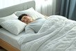 © Noufaldi - A young man peacefully sleeping in a cozy bed with soft pillows and a light blanket.