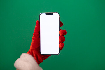 santa's hand in a red glove holding a smartphone with a blank white screen on a green background, perfect for christmas promotions or holiday app designs