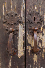 Wall Mural - Description: Two intricately designed door handles, crafted from wrought iron, adorn a weathered wooden door